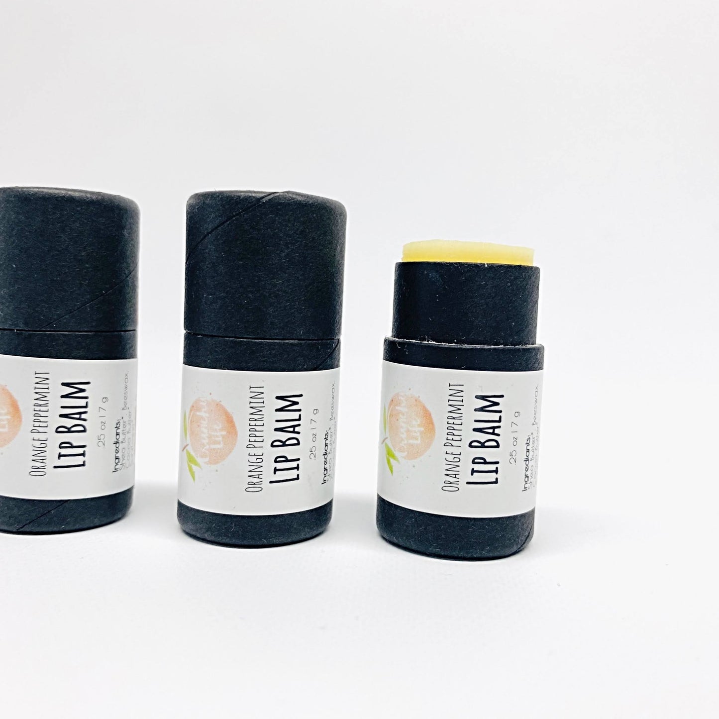 Three small, black cardboard lip balm tubes with white labels. One is without a lid.