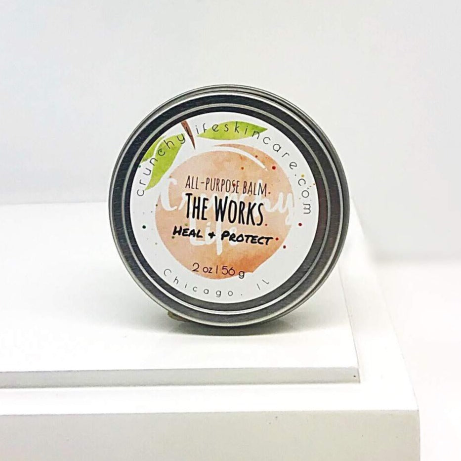 Round, silver tin with white label. Label has peach logo. The Works All-Purpose Balm