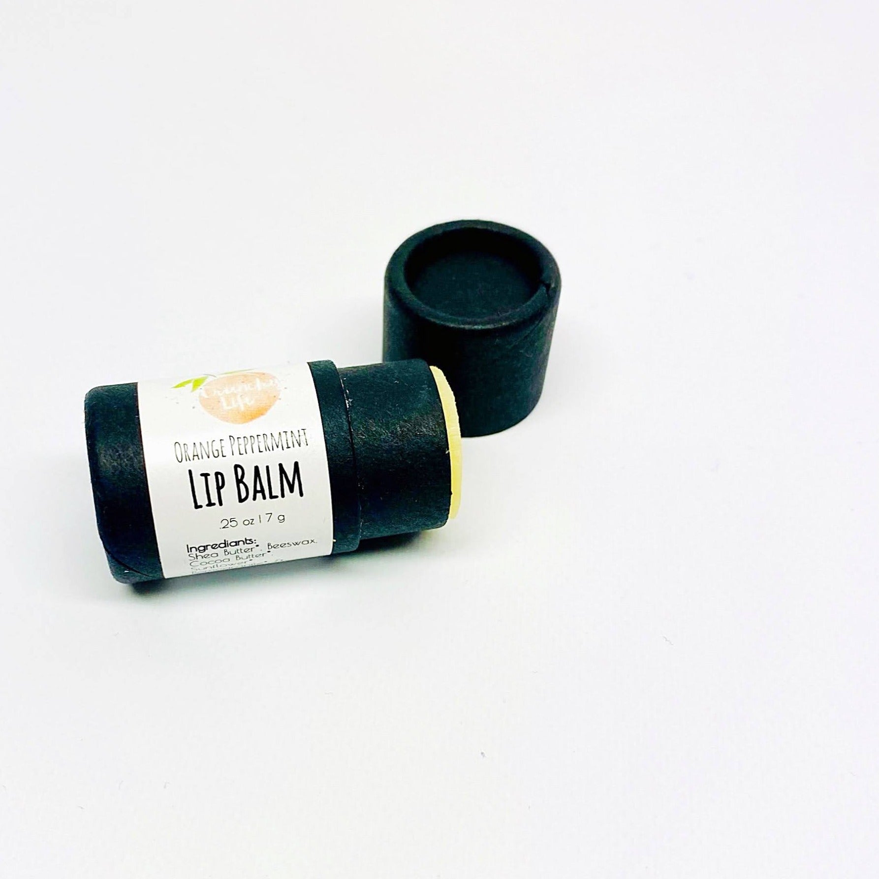 Small, black lip balm tube with white label. Lying on its side with lid off and lip balm showing.